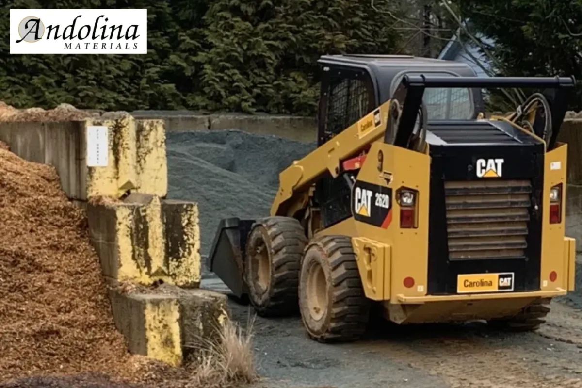 Skid steer working near mulch and gravel landscape supplies.